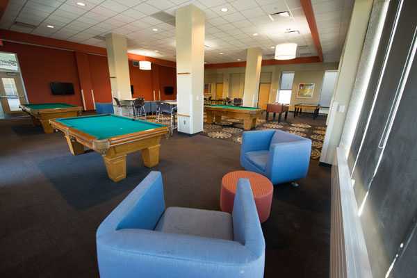 Large room with ample seating, flat screen TVs, pool tables, table tennis table, foosball table.