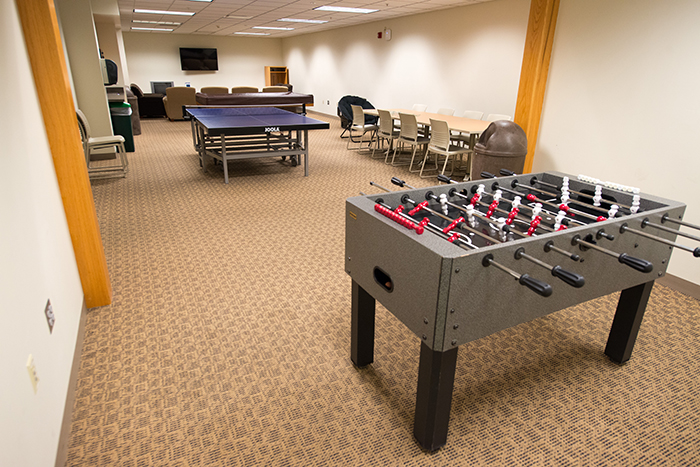 Long rectangular room with TV with seating, ping pong and Foosball tables.