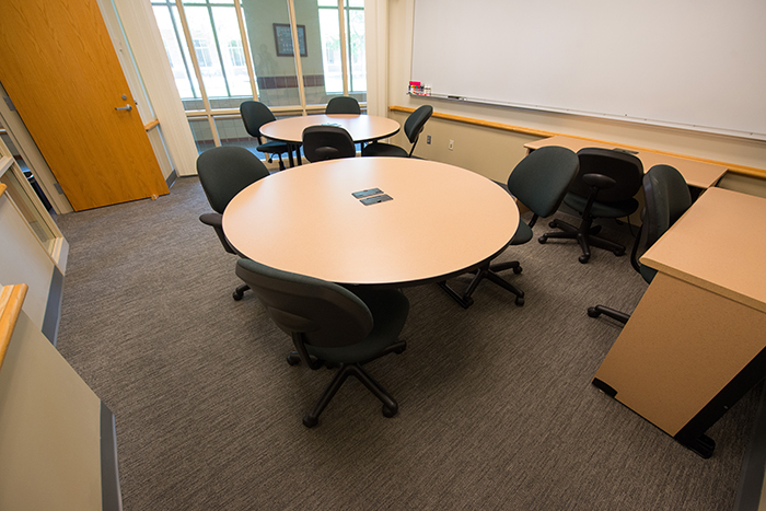 Room with two round tables, two rectangular desks and dry erase boards.